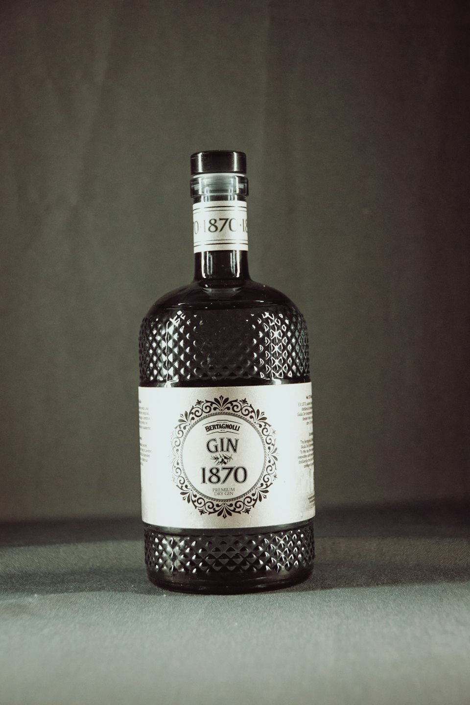 Una bottiglia di gin in vetro a rombi su sfondo grigio.