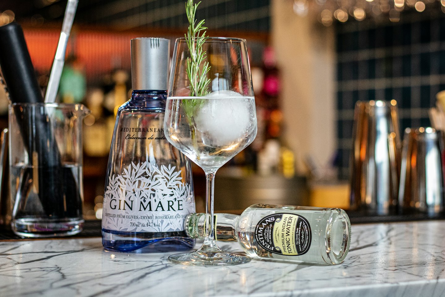 Un bicchiere di gin tonic con rosmarino su un bancone di marmo.