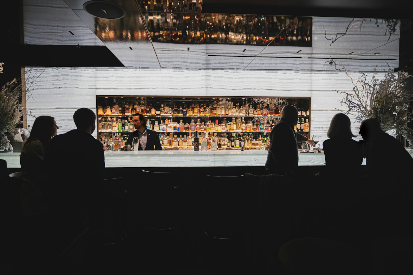 Bartender che serve clienti dietro un bancone ben fornito di liquori.