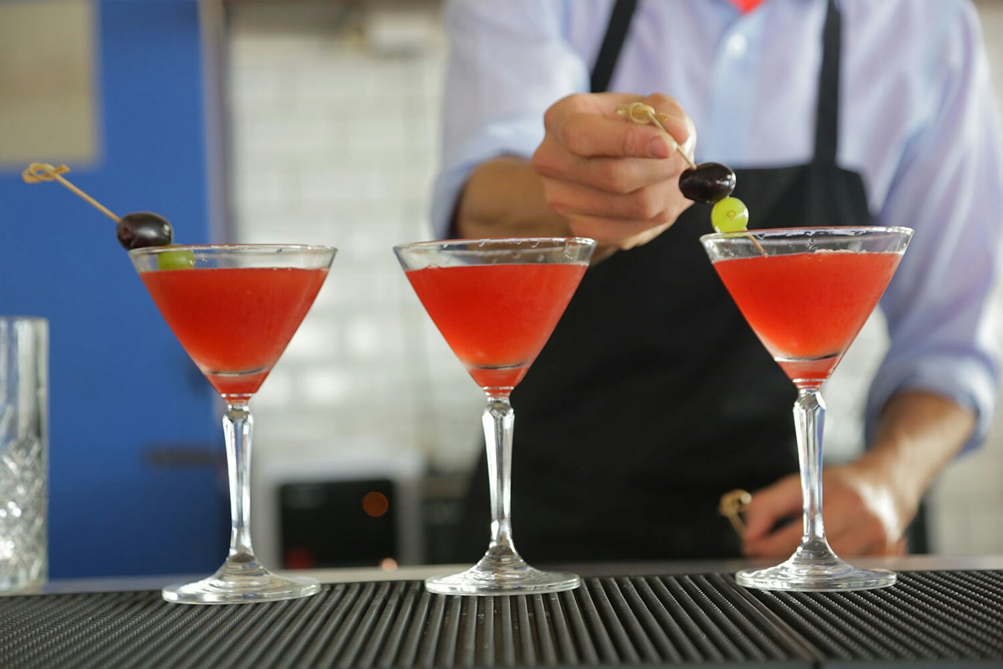 Un barista guarnisce un cocktail rosso con uva al bancone.