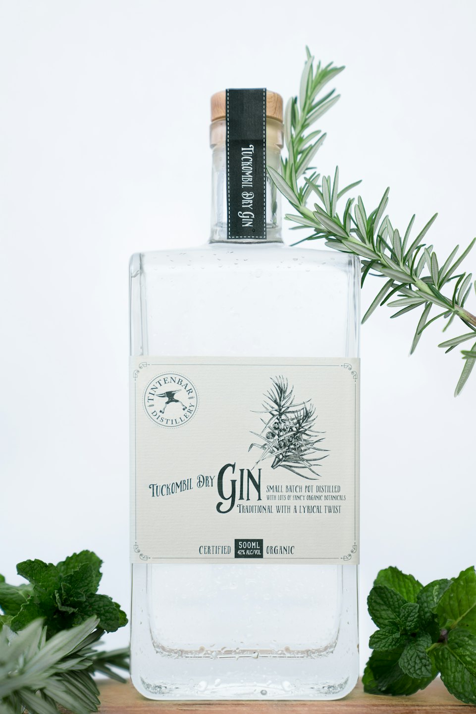 Bottiglia di gin con rosmarino e menta su una superficie di legno.